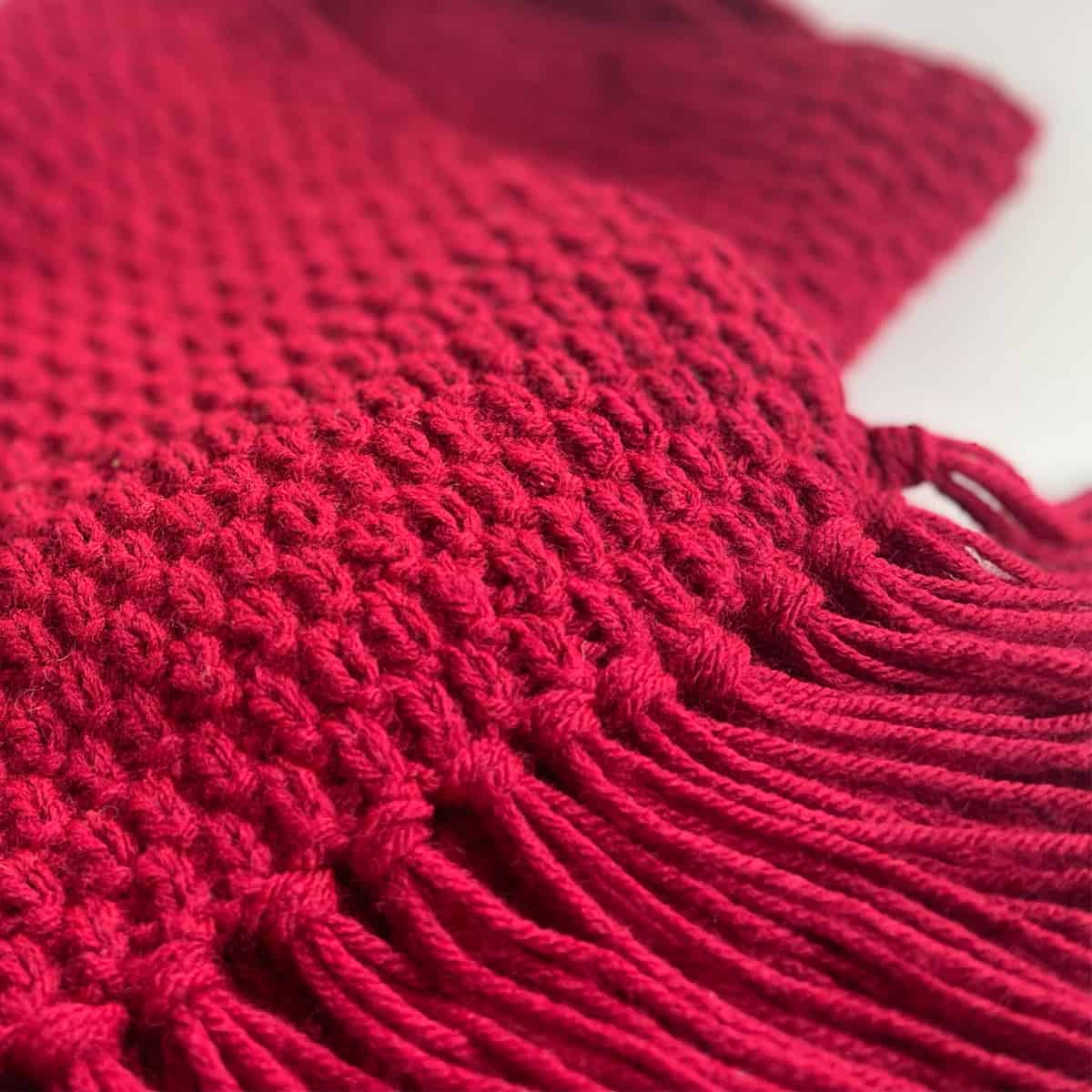 The Swift Stitch texture detail with fringe tassel edges in a red scarf.