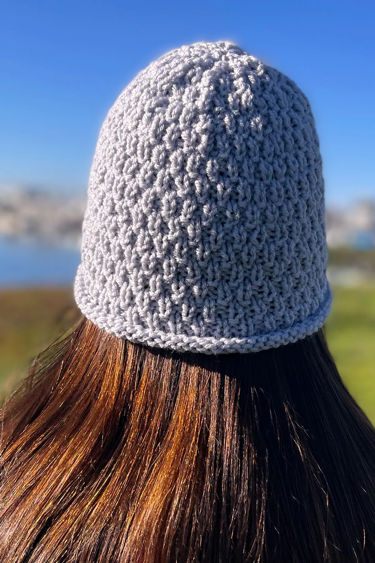 Knitted hat in Swift Stitch pattern texture with grey color yarn modeled on woman's head.