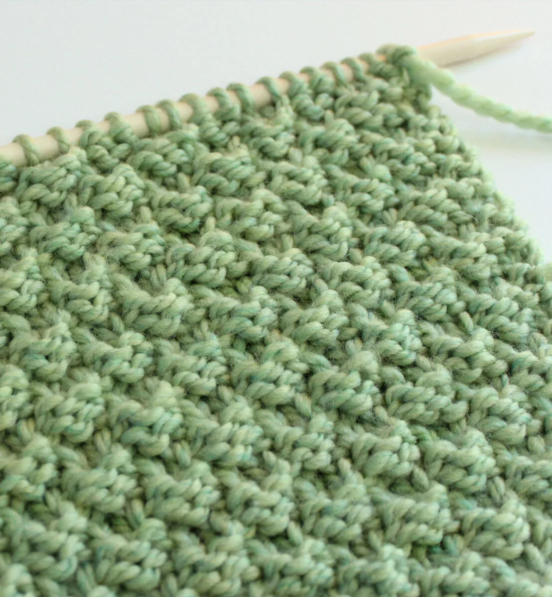 Side view of Double Moss Stitch texture on knitting needle in green color yarn.