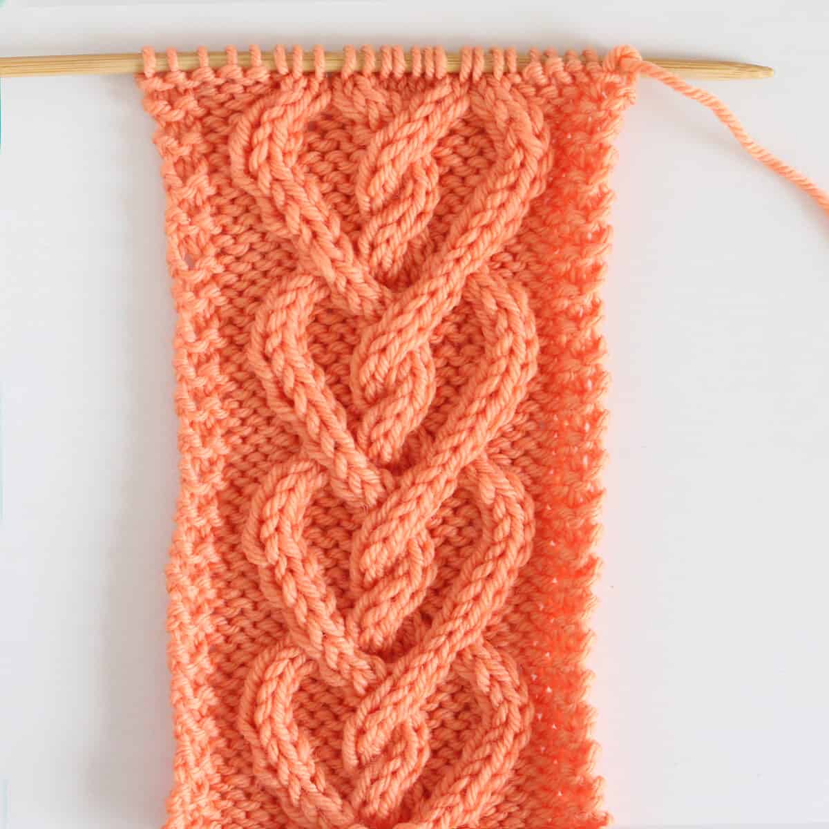 Cable Hearts knitted in orange color yarn on needle.