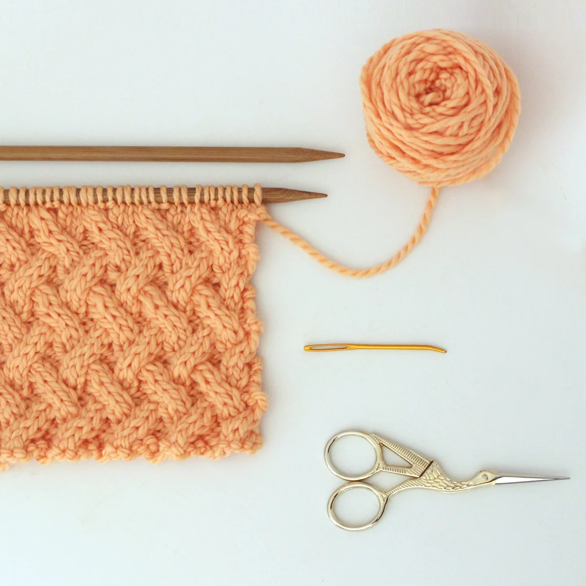 Knitting supplies for Lattice Cable Stitch with yarn, needles, scissors, and tapestry needle.