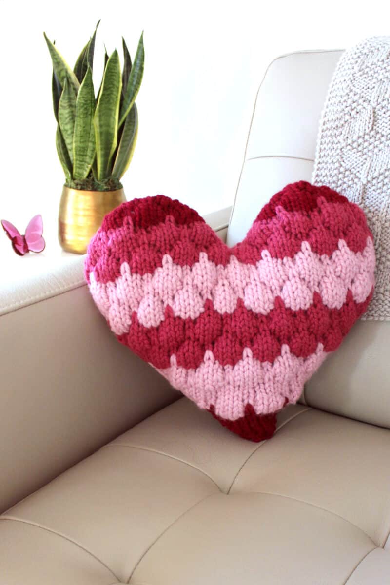 Bubble Stitch Heart Pillow on couch corner in red and pink yarn colors.