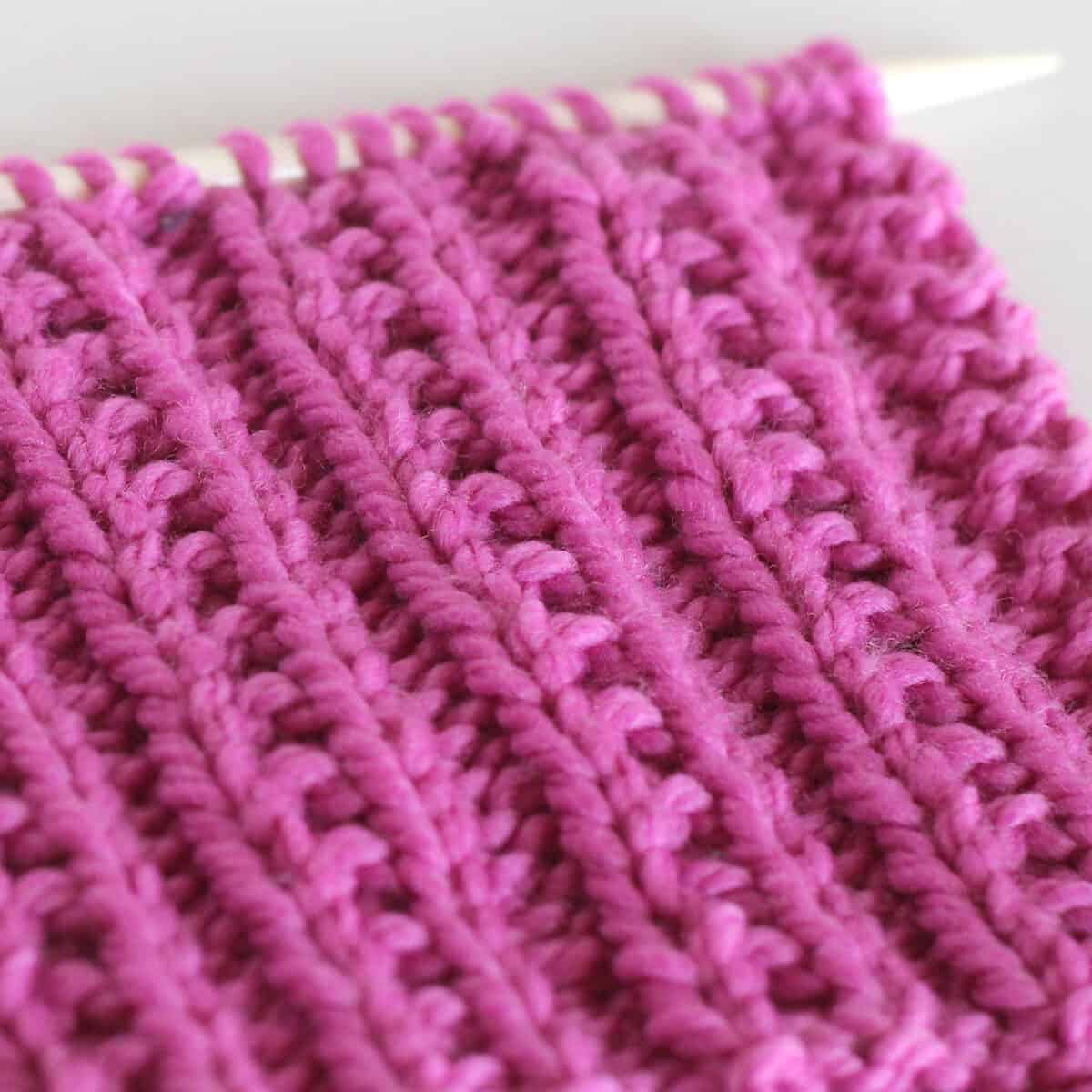 Side texture view of Beaded Rib Knit Stitch Pattern in pink color yarn on knitting needle.