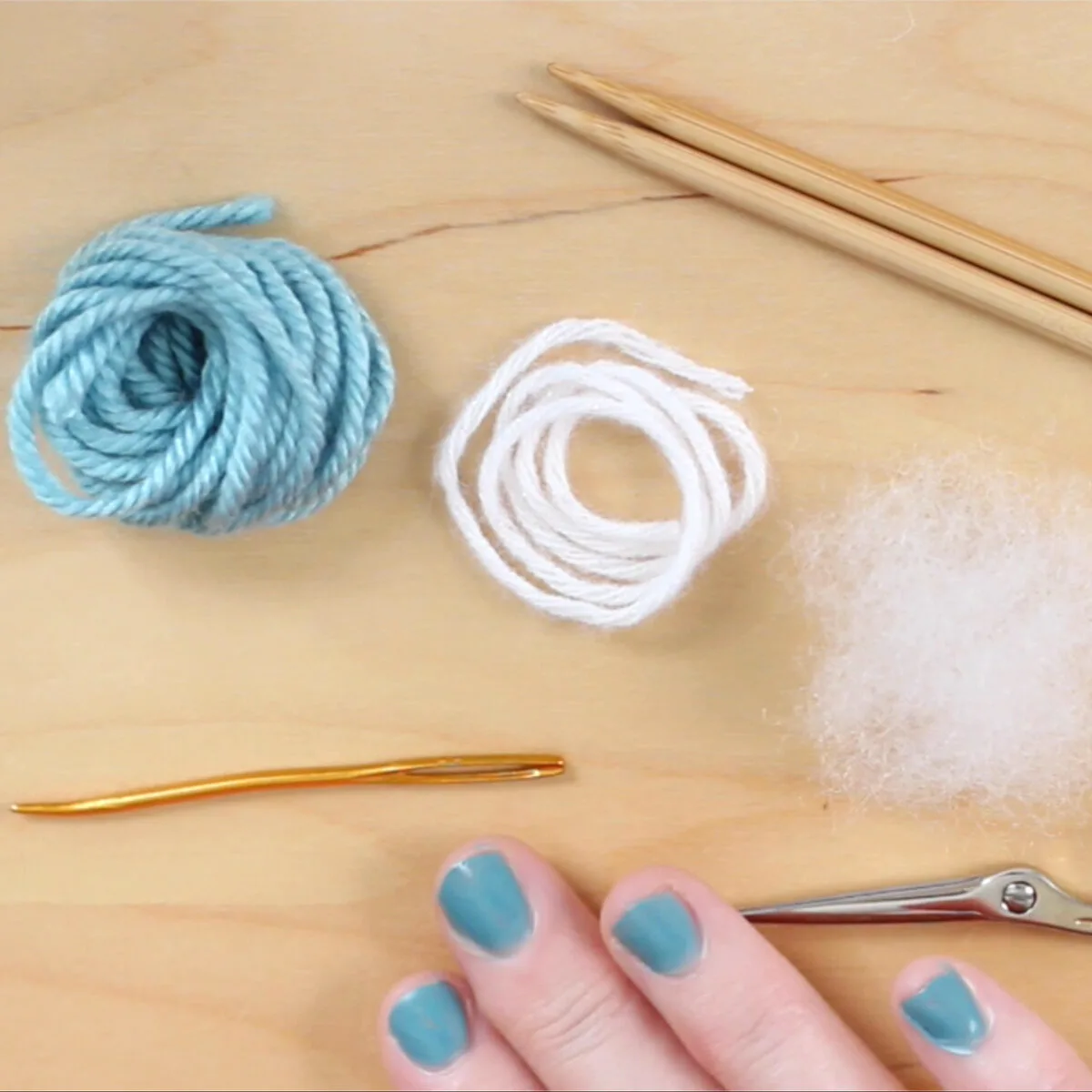 Knitting supplies of light blue yarn color, knitting needles, scissors, and a tapestry needle.