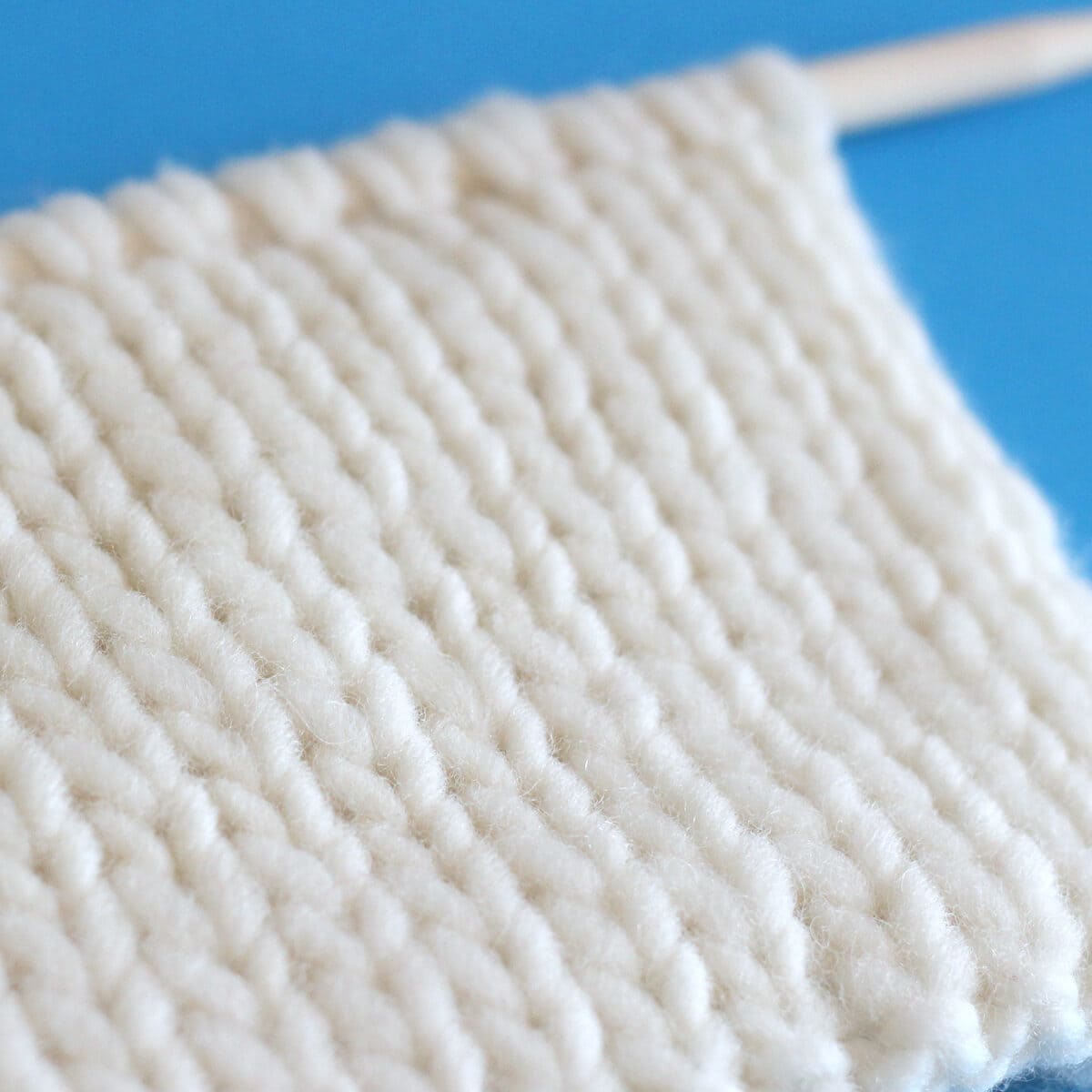 Close up of the side of the Double Stockinette stitch on straight knitting needles in white yarn.