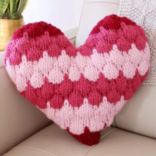 Bubble Stitch Heart Pillow on couch corner in red and pink yarn colors.