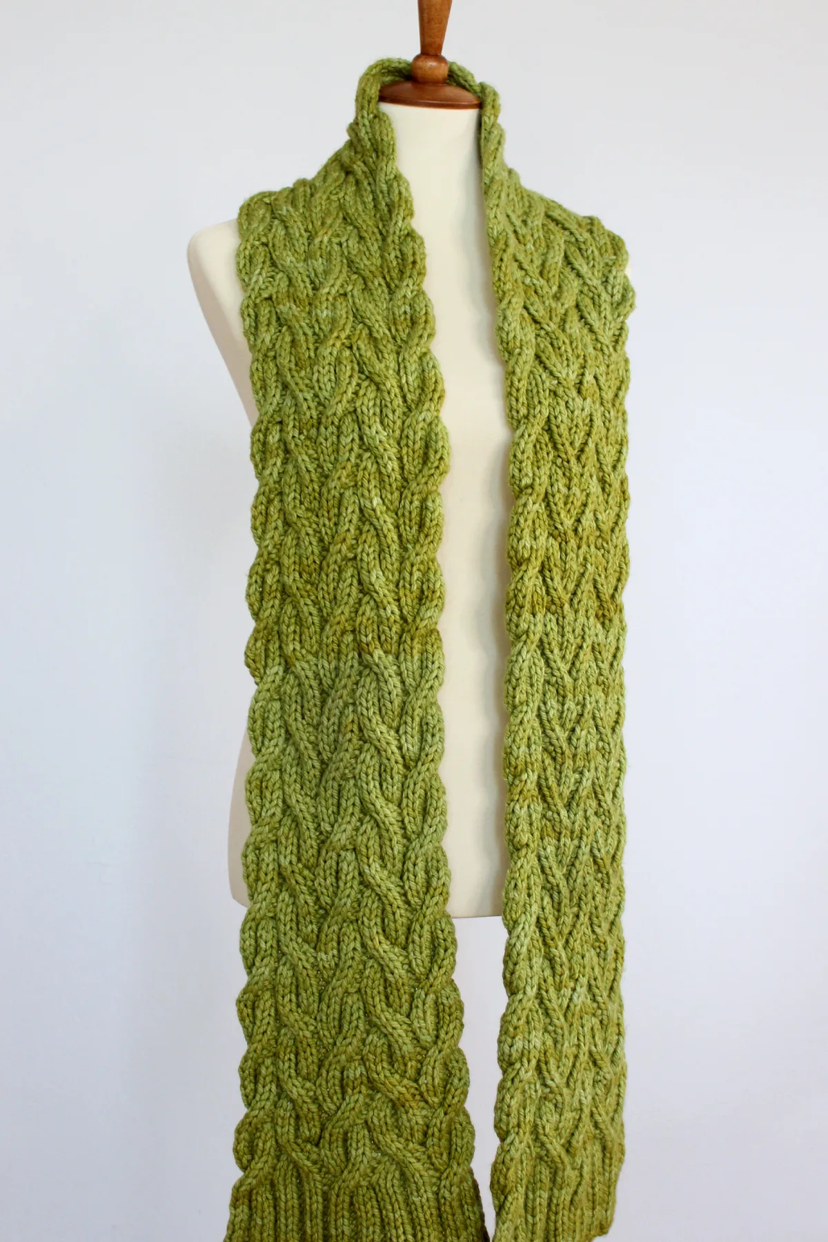 Long Reversible Cable Scarf in green yarn on mannequin designed by Studio Knit.