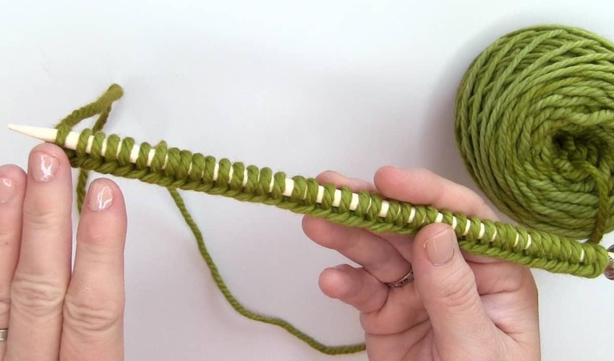 Cast On 40 Stitches of green bulky weight yarn onto a white knitting needle.