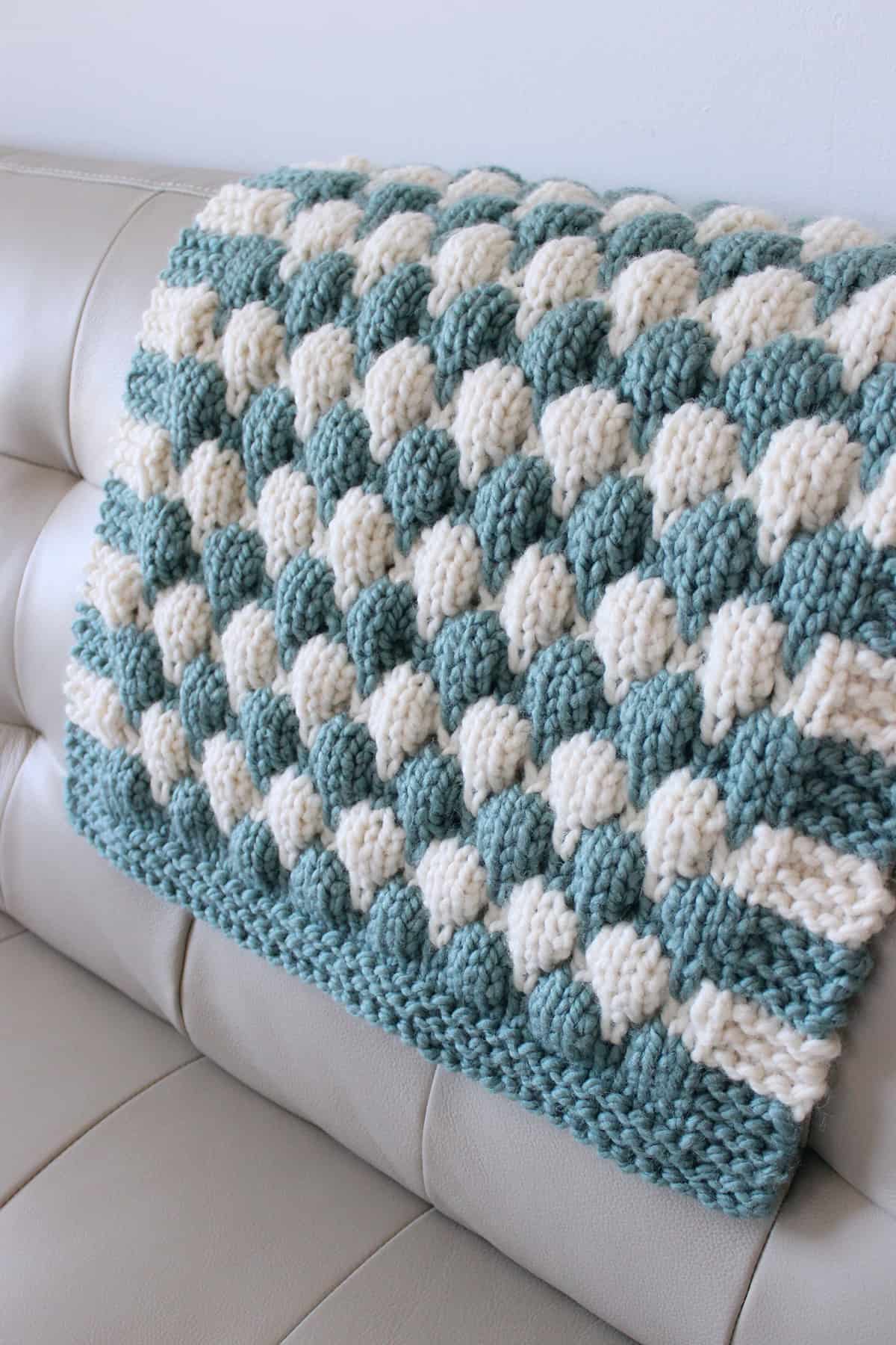 Chunky baby blanket in blue and white yarn colors on couch.