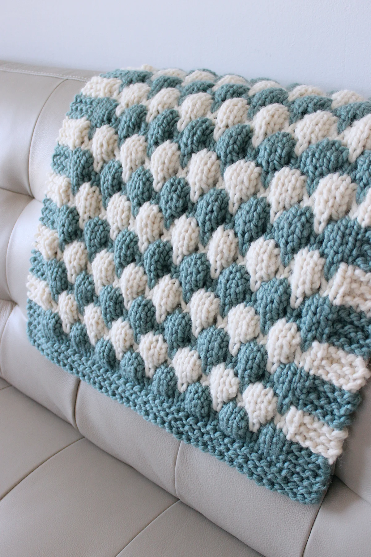 Chunky baby blanket in blue and white yarn colors on couch.