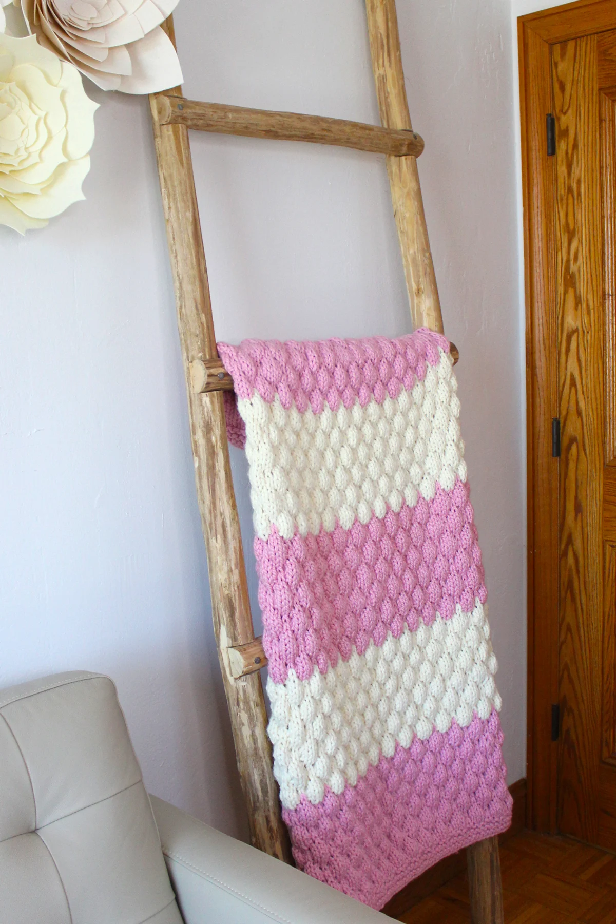 Chunky bubble stitch blanket in pink and white yarn colors displayed on rustic ladder.