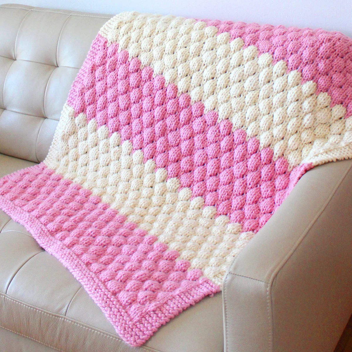 Bubble Stitch Blanket knitted with pink and white yarn colors on a couch.