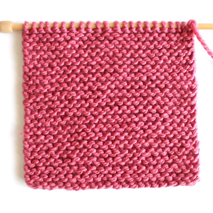 Garter stitch knitted flat on straight knitting needles in pink color yarn.