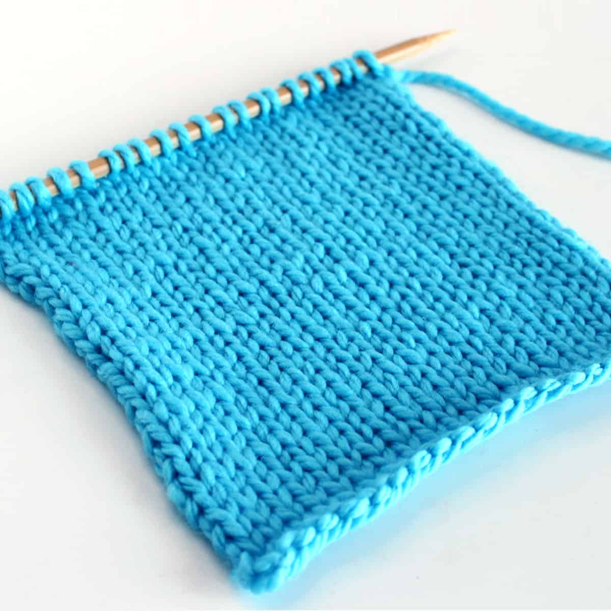 Stockinette Stitch flat on knitting needle in blue color yarn.