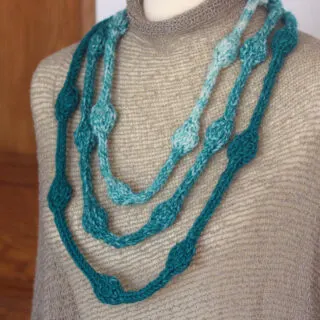 Close-up of a Necklace with Beaded Texture knitted in blue and white yarn colors worn on a torso.