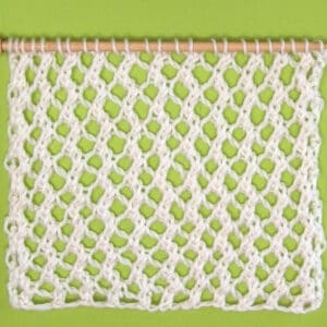 Easy Mesh Lace Knitting Pattern swatch sample in white yarn color on needle atop a green background.