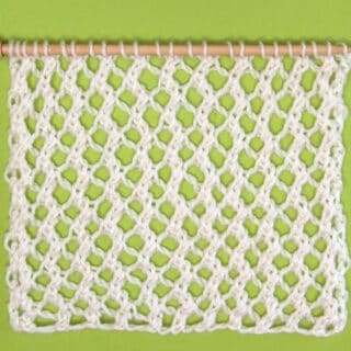 Easy Mesh Lace Knitting Pattern swatch sample in white yarn color on needle atop a green background.