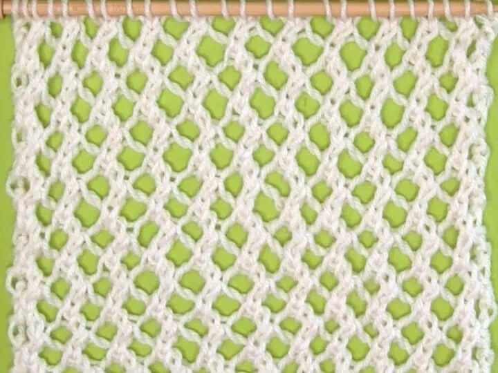 Easy Mesh Lace Knitting Pattern swatch sample in white yarn color on needle atop a green background.