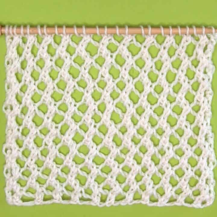 Easy Mesh Lace Knitting Pattern swatch sample in white yarn color on needle atop a green background.