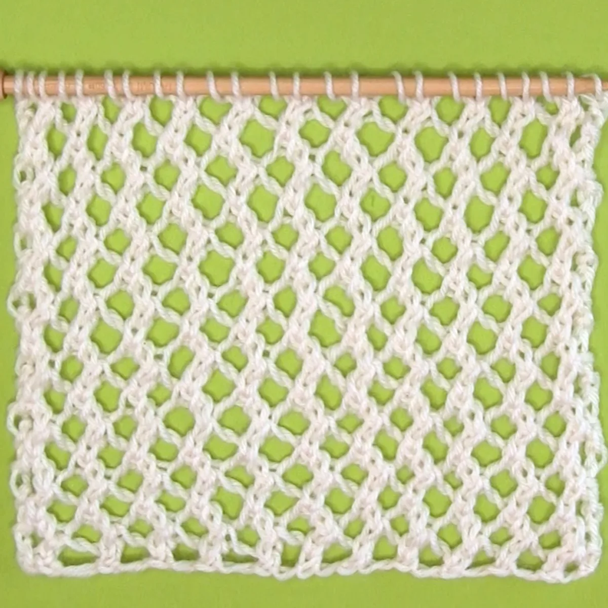 Easy Mesh Lace Knitting Pattern swatch sample in white yarn color on needle atop a green background.