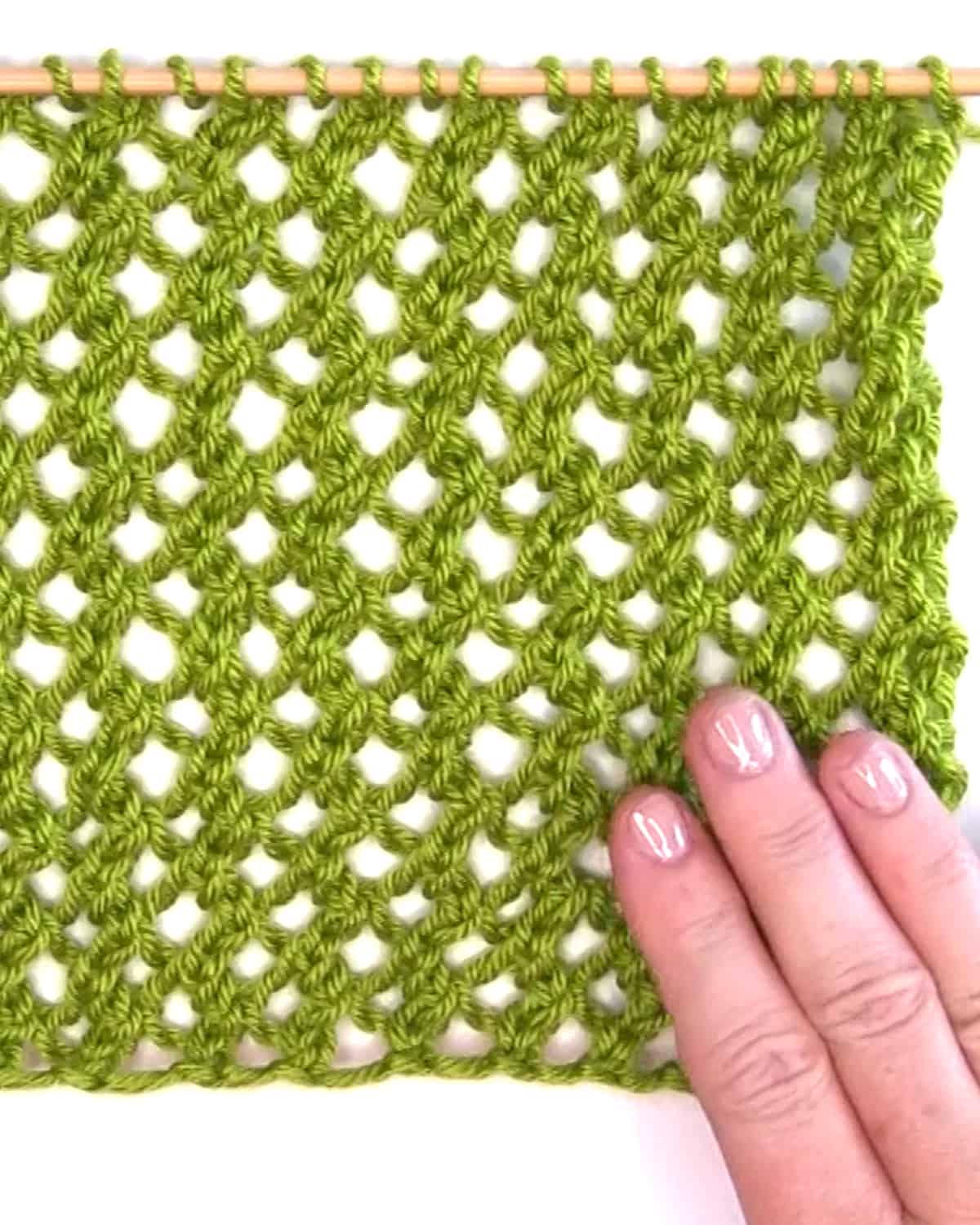 Lace knitted mesh swatch in green yarn color with hand on needle.