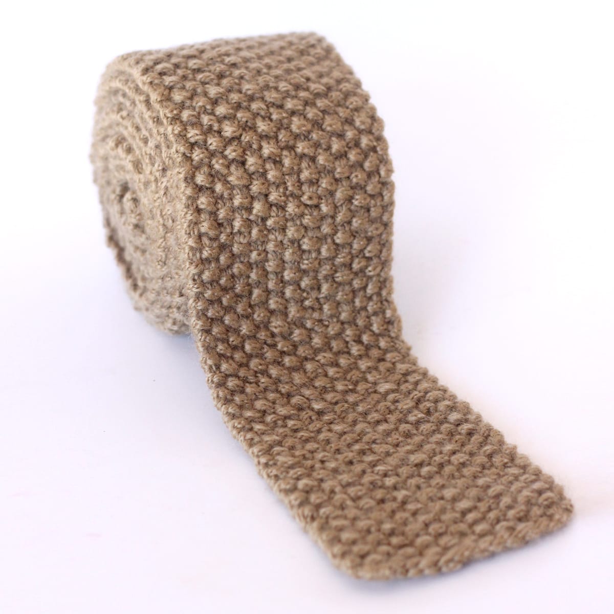 Seed Stitch Necktie knitted in tan color yarn rolled up on white background.