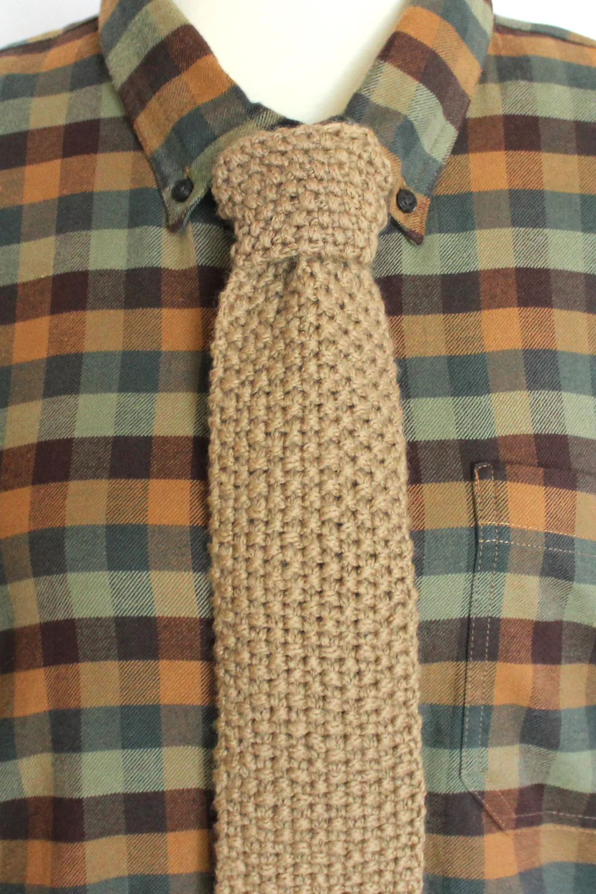 Knitted necktie in tan color worn on green and brown checkered shirt.