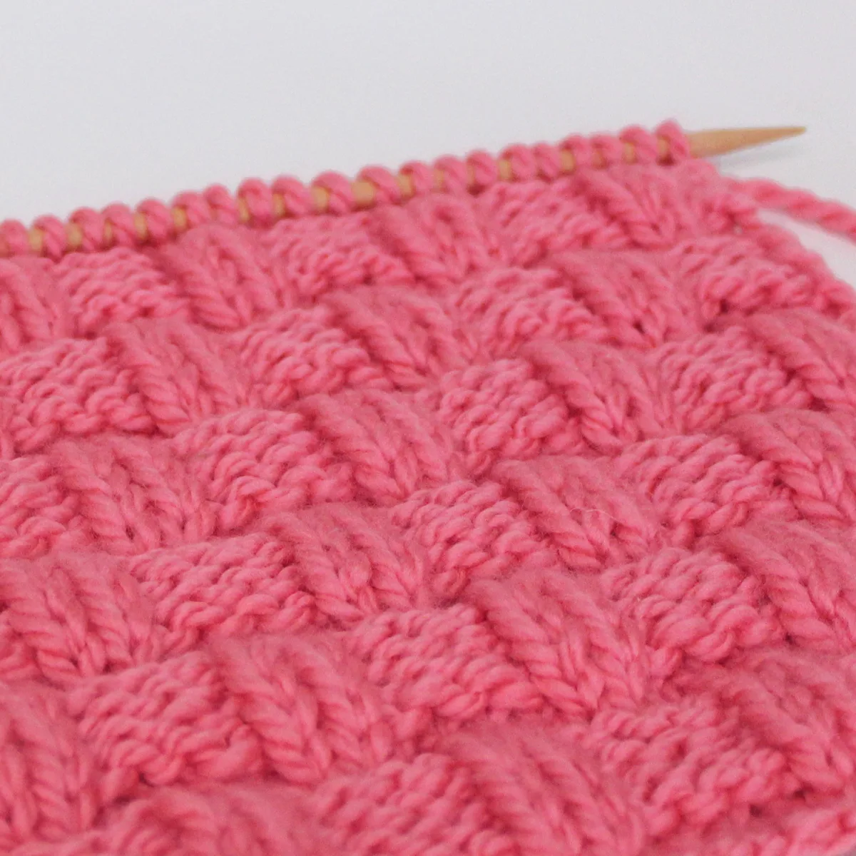 Knit stitch pattern in basket weave texture in pink yarn color on knitting needle.