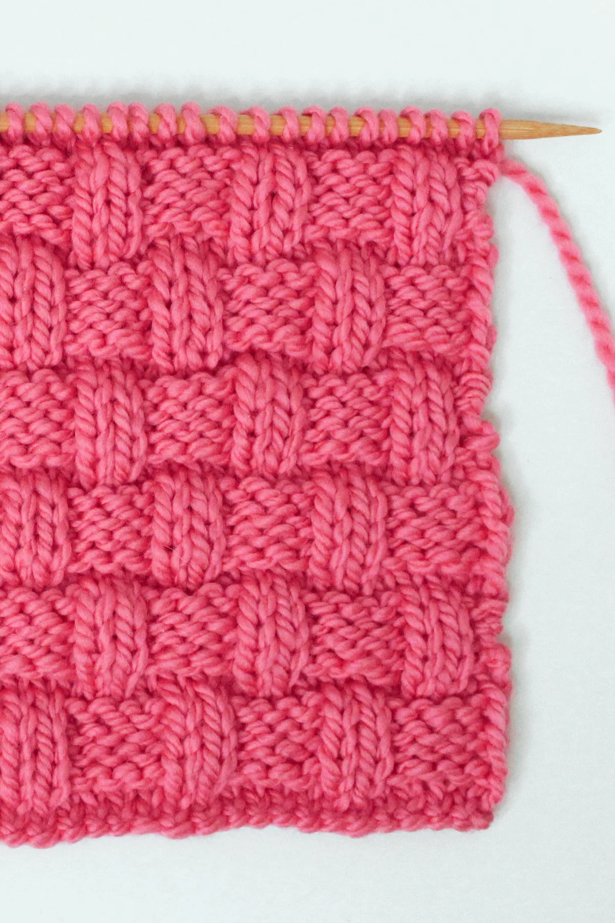 Basket Weave stitch pattern on knitting needle in pink color yarn.