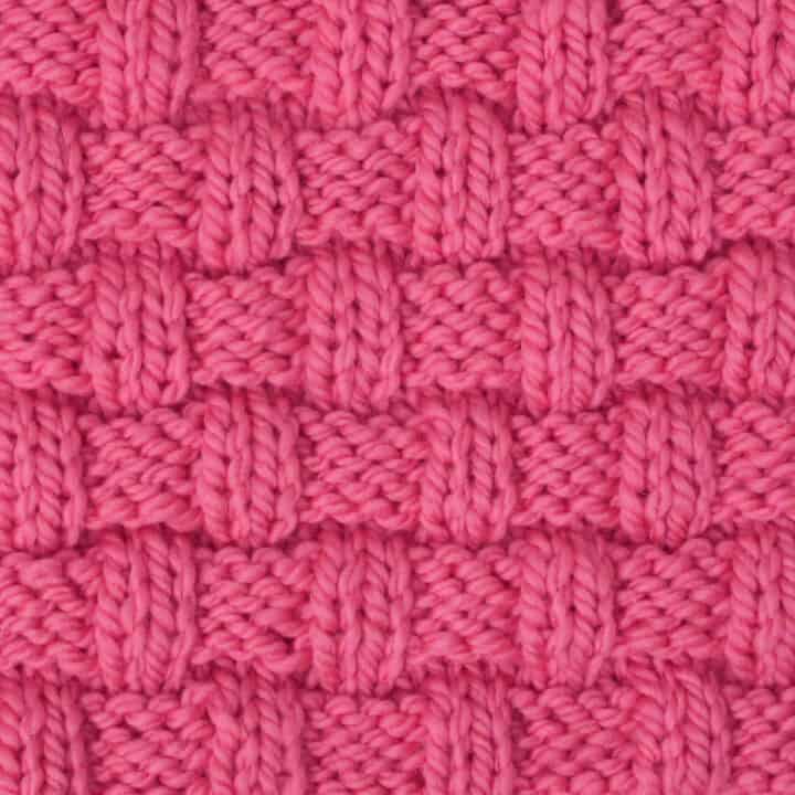 Basket Weave stitch pattern on knitting needle in pink color yarn.