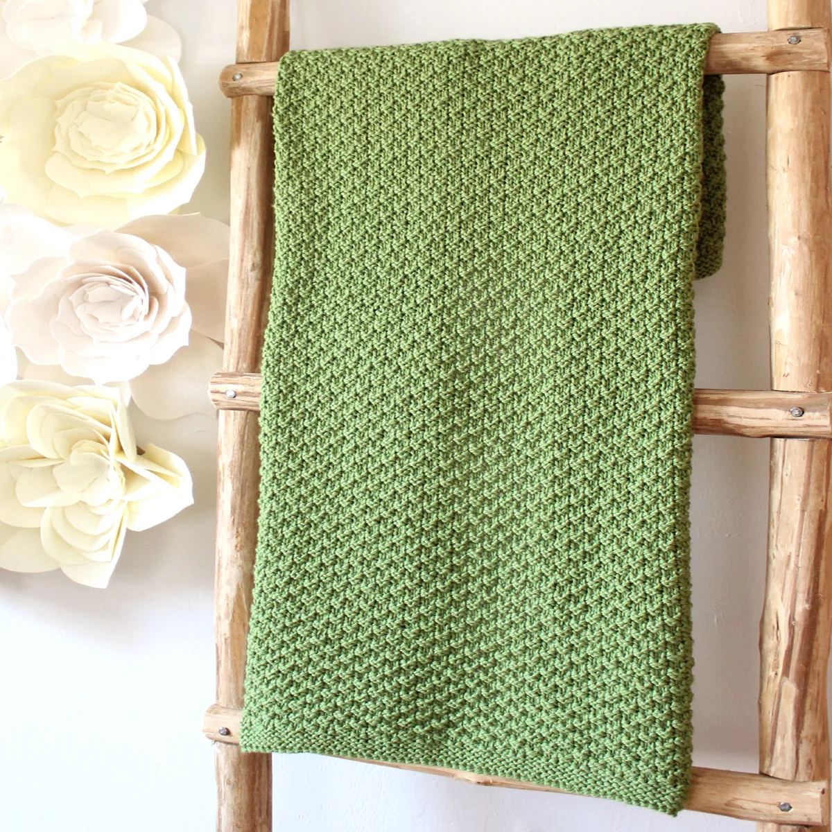 Wooden ladder with Moss Landing knitted blanket by Studio Knit in green yarn color.