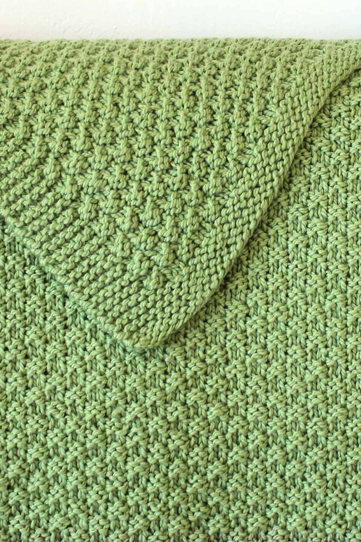 Reversible knitted blanket in double moss stitch pattern with green yarn color.