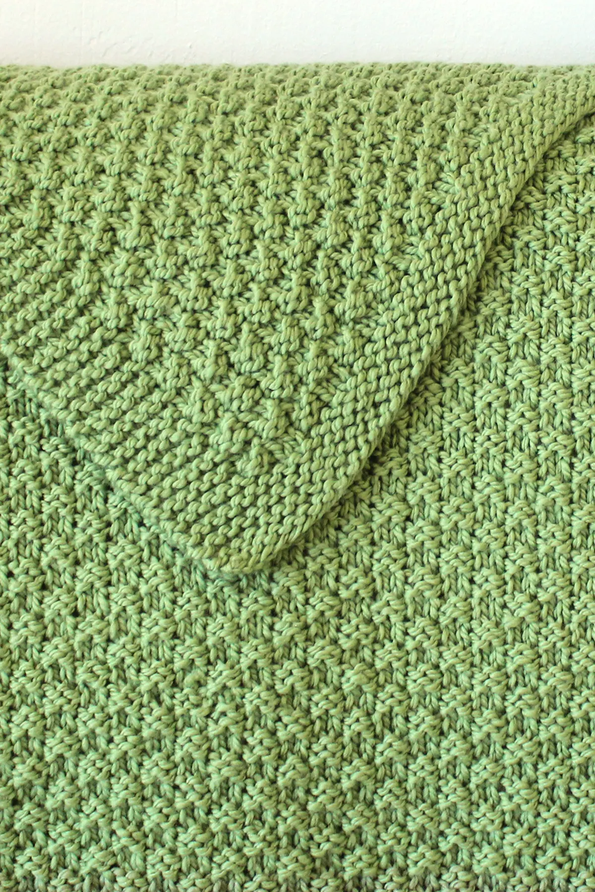 Reversible knitted blanket in double moss stitch pattern with green yarn color.