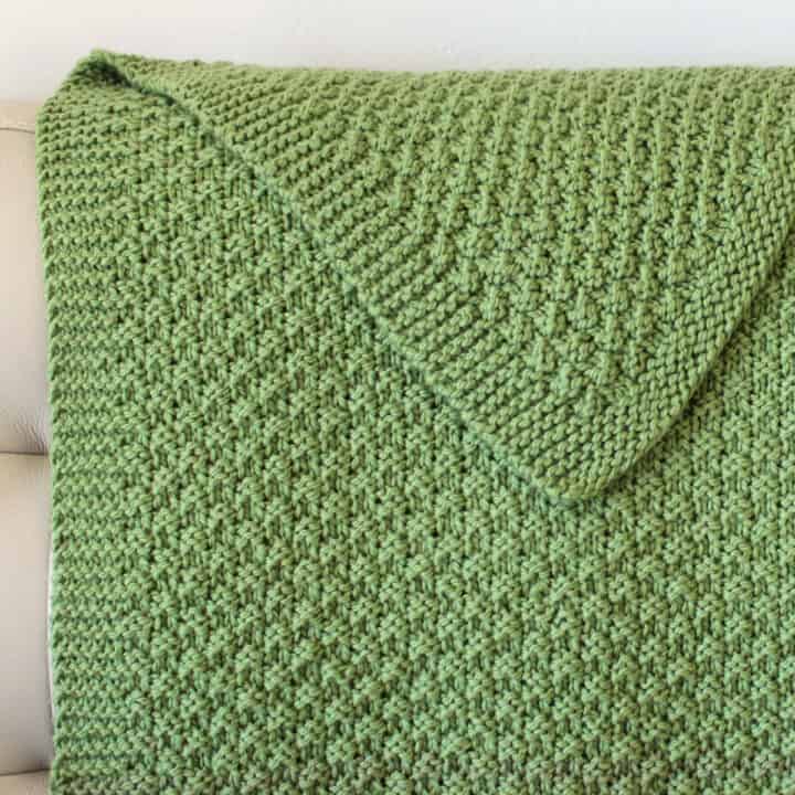 Knitted blanket on couch in green yarn color with reversible texture in double moss stitch.