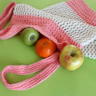Knitted mesh market bag in peach and white yarn colors filled with fruit.