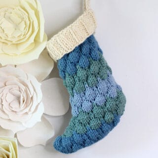 Knitted Bubble Stocking in shades of blue yarn and a cream color cuff on wall with felt flowers.