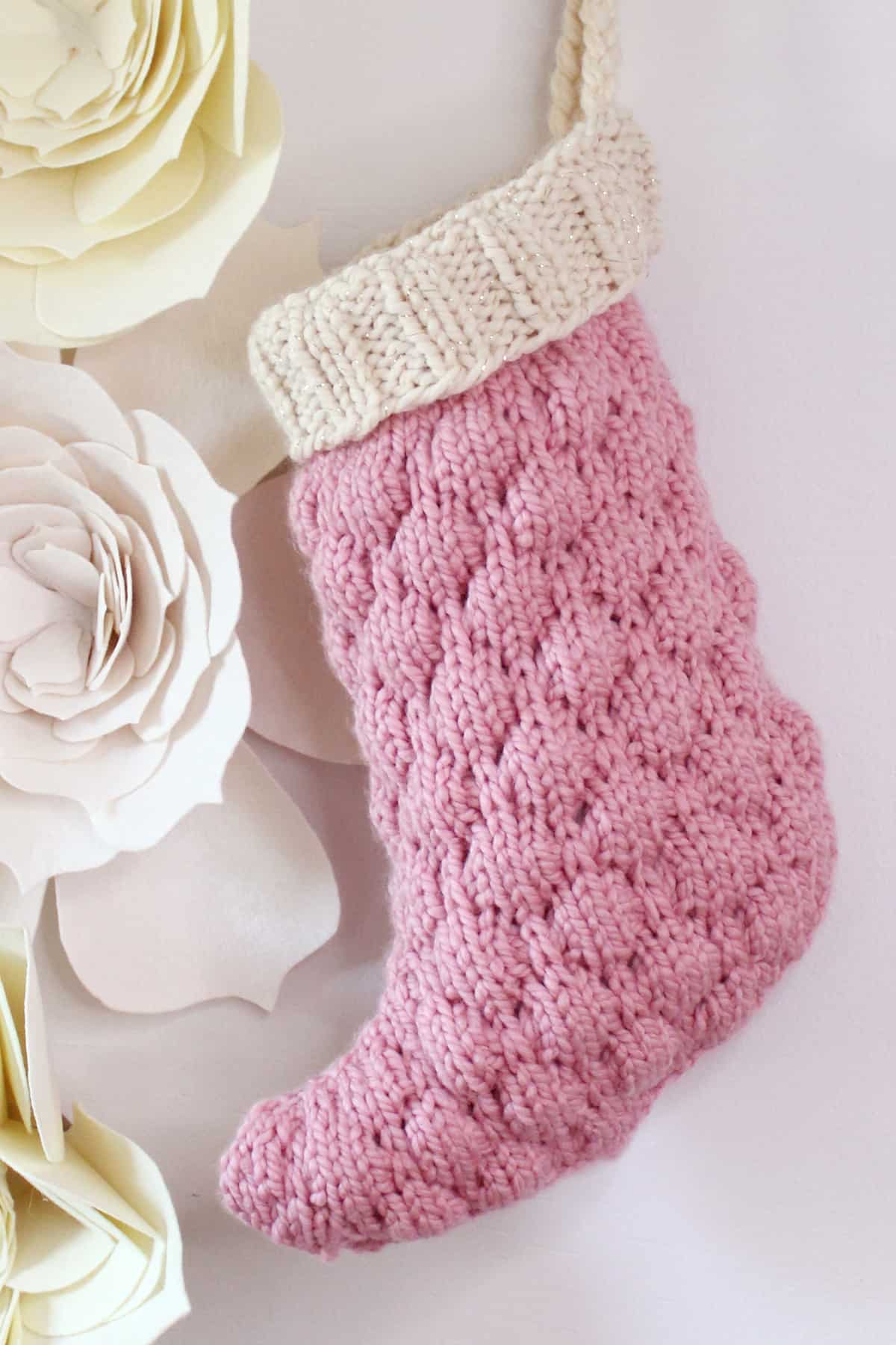 Knitted Bubble Stocking in pink color yarn and a cream color cuff on a wall with felt flowers.