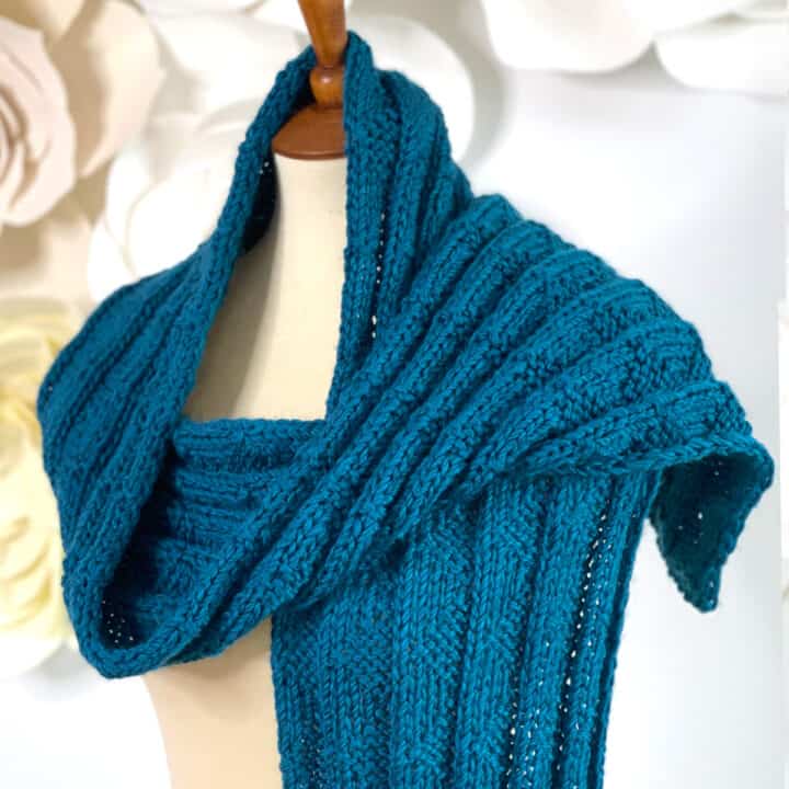 Knitted Pennant Pleating scarf wrapped on mannequin in blue color yarn.