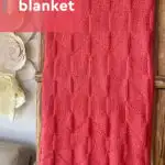Point Reyes Blanket designed by Studio Knit in coral colored yarn displayed on ladder.