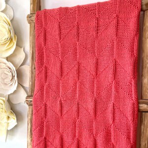 Parallelogram Blanket in coral colored yarn displayed on ladder.