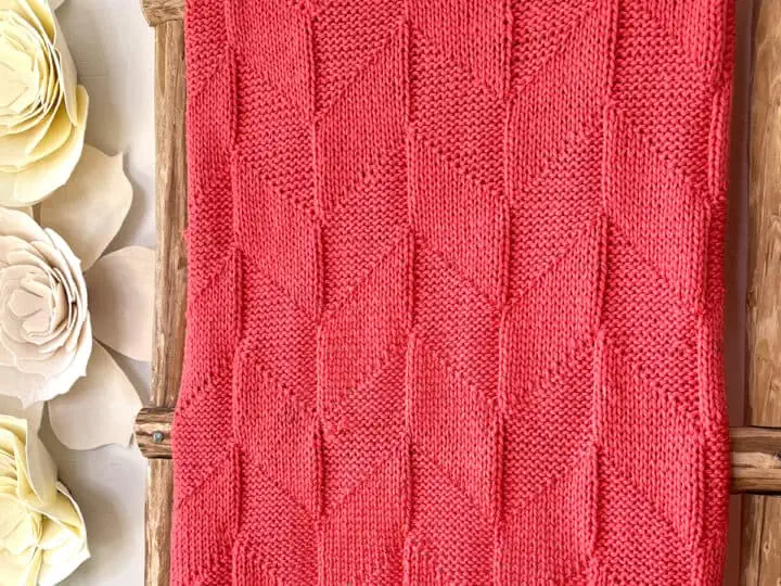 Parallelogram Blanket in coral colored yarn displayed on ladder.