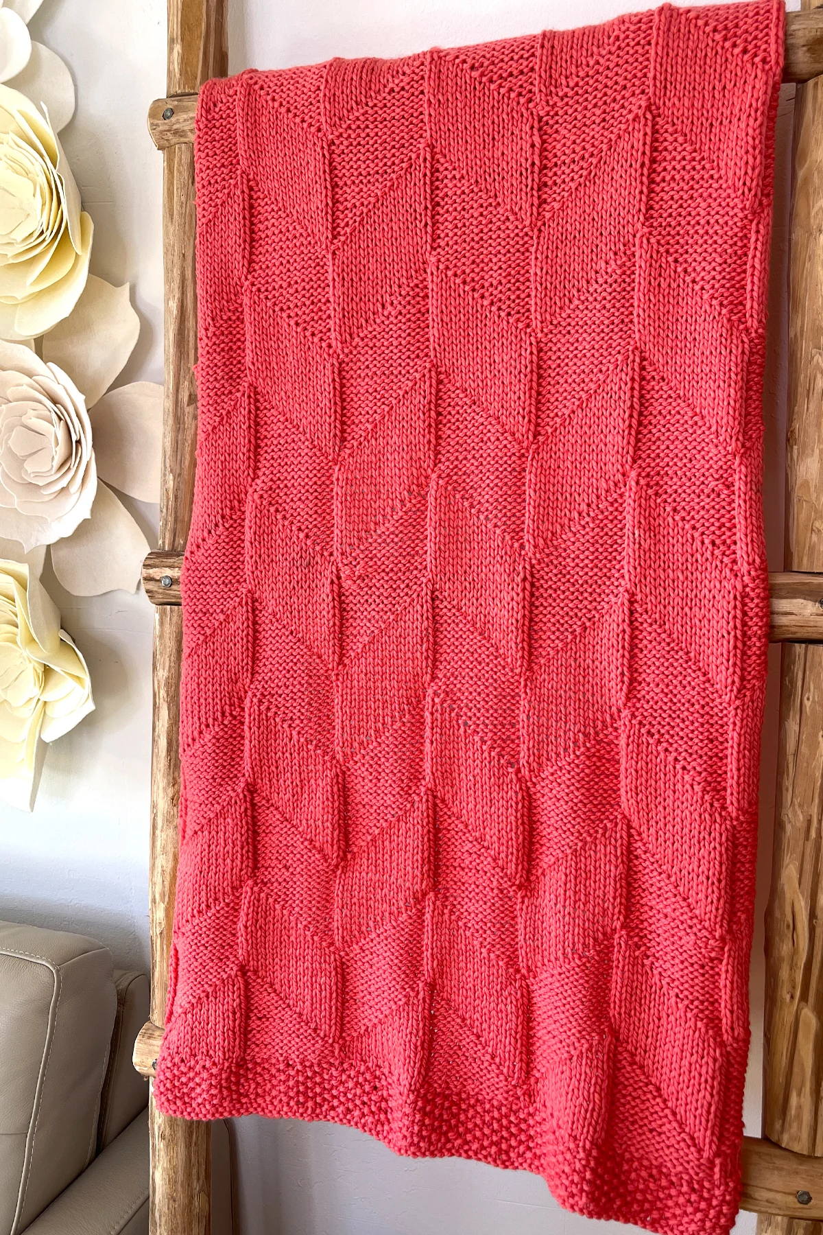 Parallelogram Blanket in coral colored yarn displayed on wooden ladder.