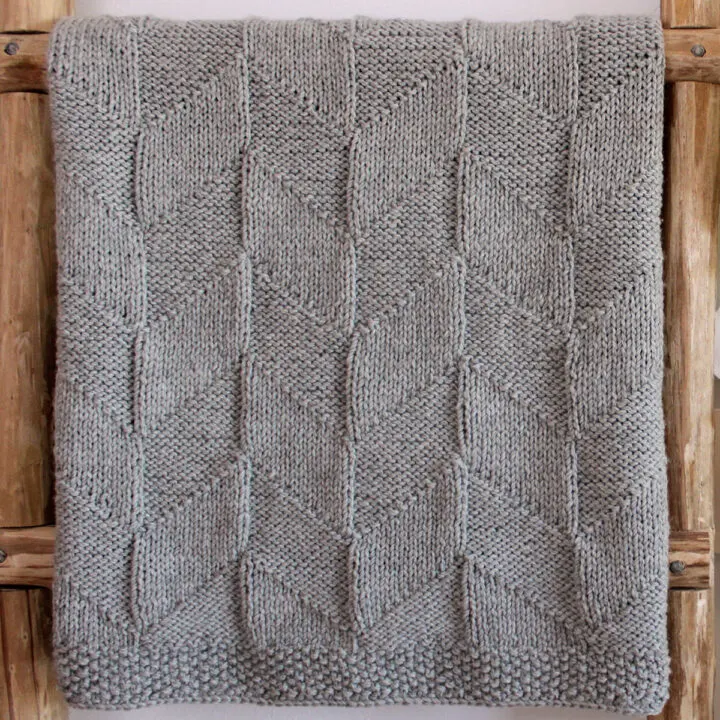 Point Reyes Blanket designed by Studio Knit in grey colored yarn displayed on ladder.