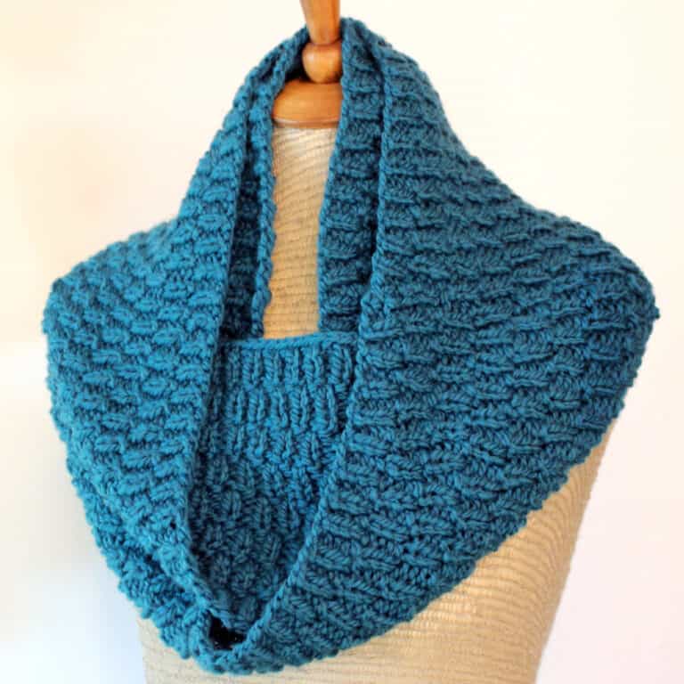 Knitted infinity scarf on mannequin in blue yarn with Long Raindrops texture.