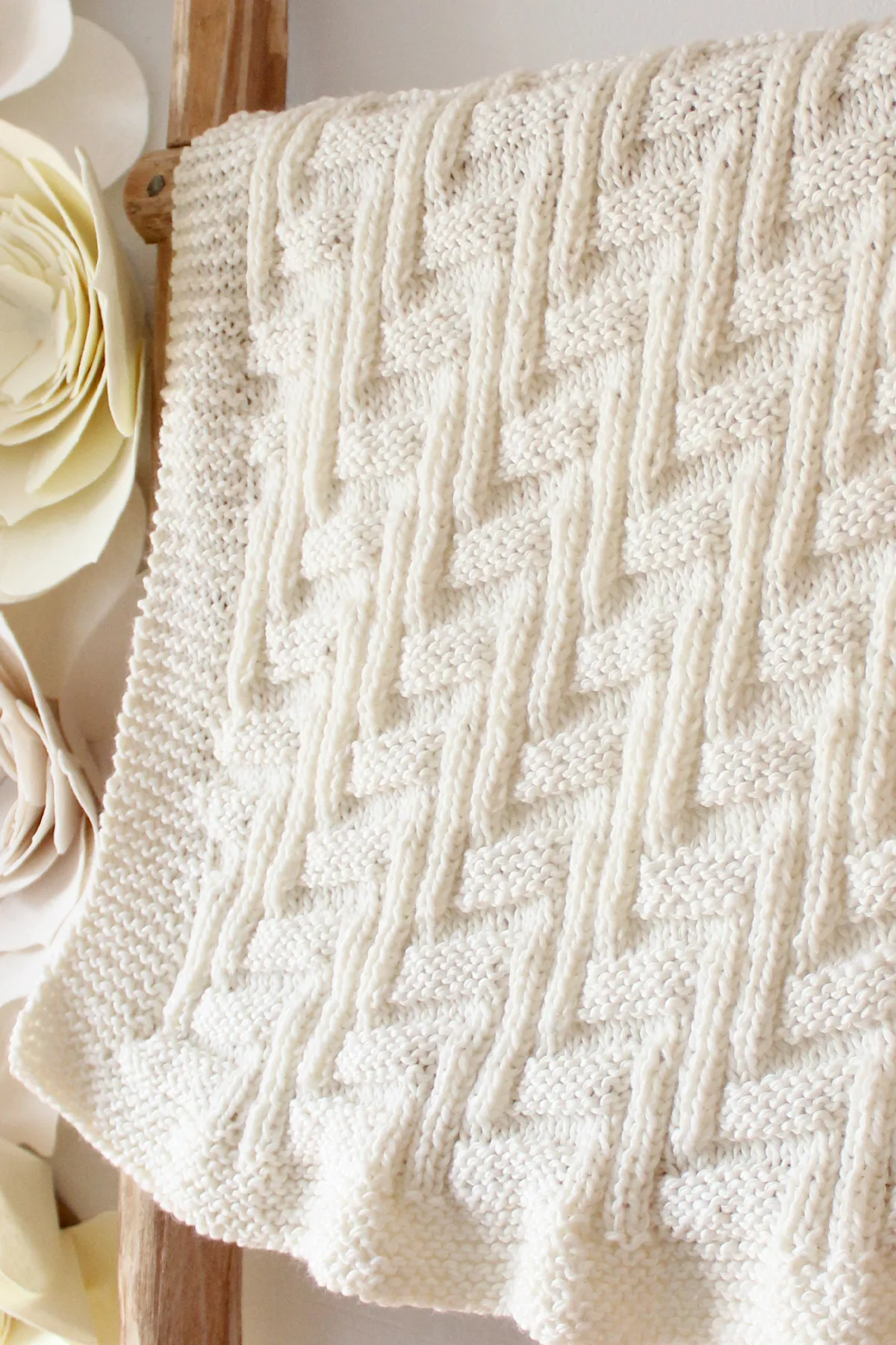 Knitted Blanket in zigzag stitch texture displayed on a wooden ladder in white yarn color.