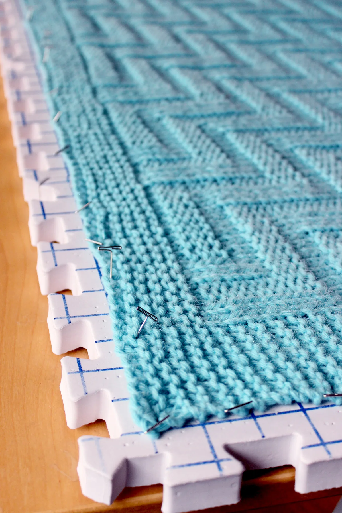 Knitted blanket pinned on blocking mats in blue yarn color.