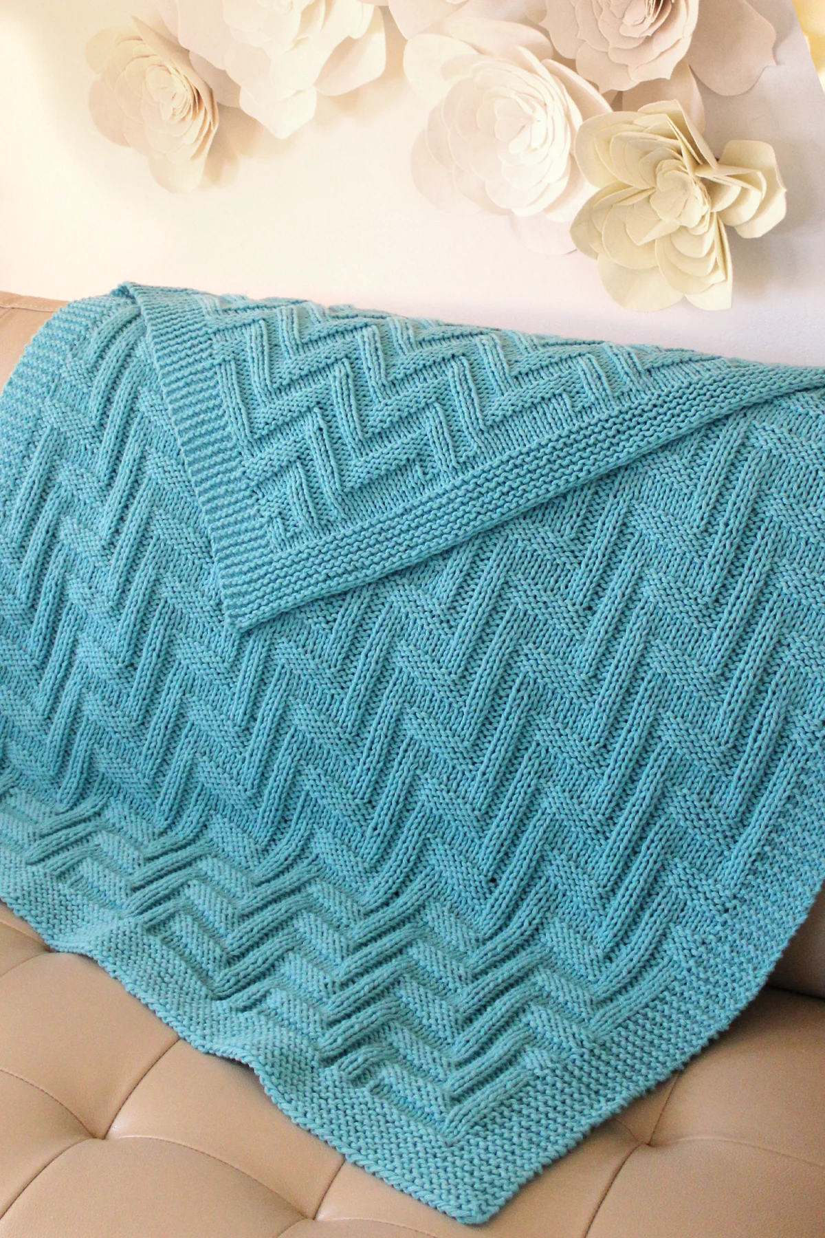 Blue knitted blanket in zigzag texture on beige leather couch.