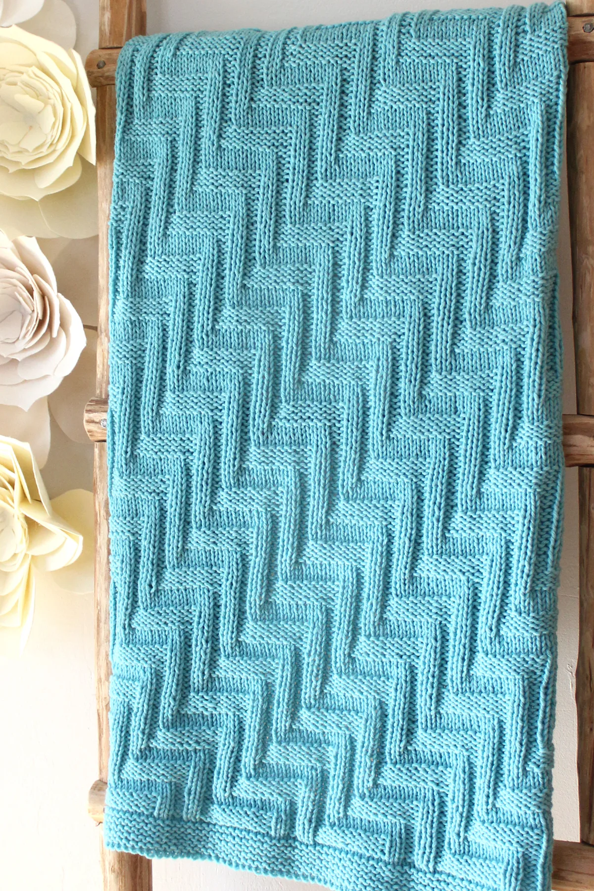 Knitted Blanket in zigzag stitch texture on wooden ladder in blue yarn color.