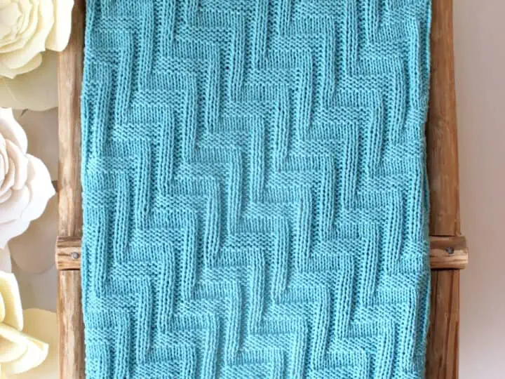 Knitted Blanket in zigzag stitch texture displayed on a wooden ladder in blue yarn color.