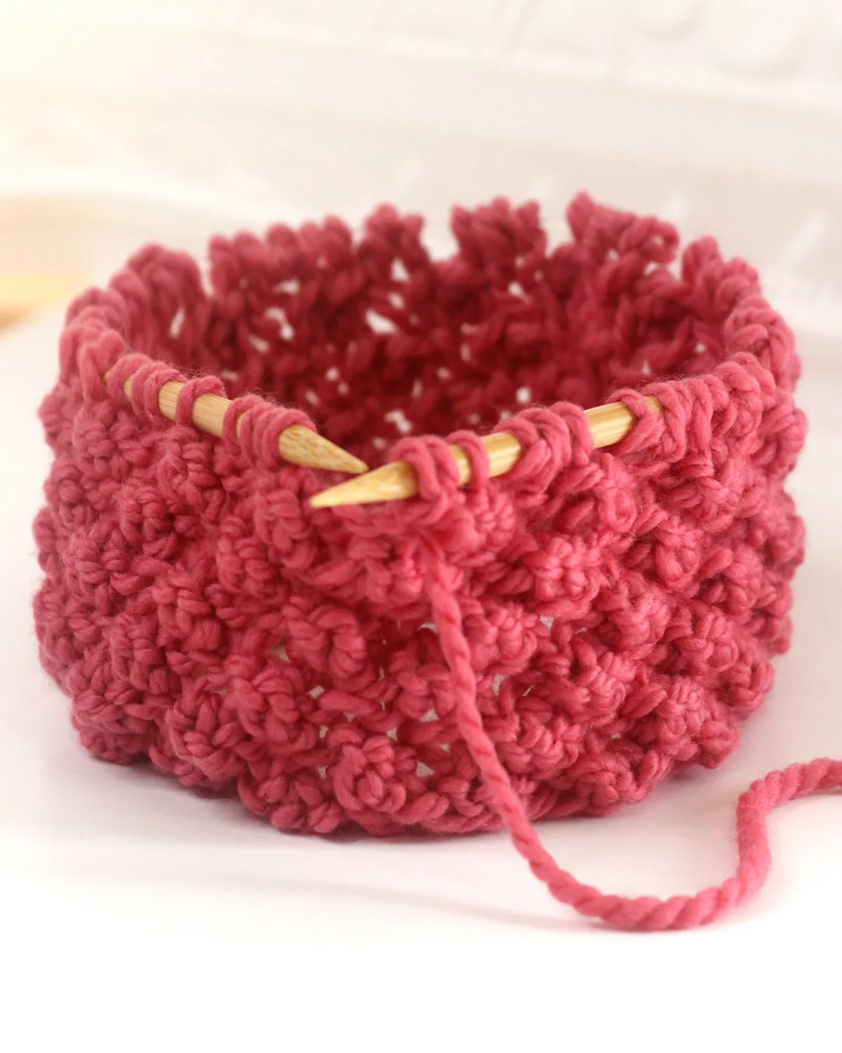 Raspberry knit stitch on circular bamboo needles with dark pink colored yarn.